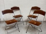three folding chairs with brown cushions sit against a white wall