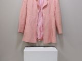 Une veste en tweed rose Chanel et une chemise rose exposées dans une boîte blanche