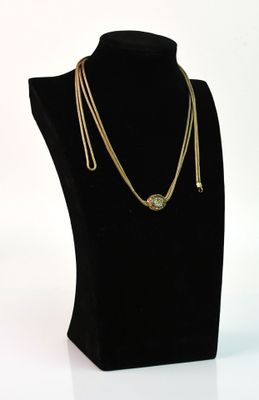 collier composé d'une chaîne en or et d'une pierre verte, présenté sur un mannequin noir