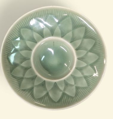 un bol vert orné d'une fleur, posé sur un fond blanc