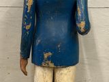 an old wooden figure of a man in a blue jacket and white pants