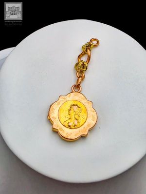 une plaque blanche à laquelle est attaché un porte-clés doré orné d'un médaillon doré