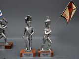 three silver figurines of soldiers holding flags on wooden bases