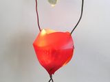 une lampe rouge posée sur un pied, sur une surface blanche
