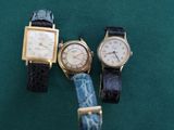 Trois montres sont posées sur un tissu vert, sur fond vert.