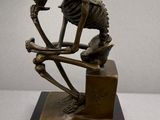 statue of a skeleton sitting on a block with a skull on it ' s head