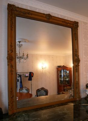 un grand miroir au milieu d'une pièce, avec un lustre en arrière-plan
