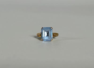 une image d'une bague en topaze bleue posée sur une surface blanche