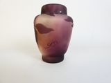 un vase violet orné d'un oiseau, posé sur une surface blanche