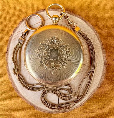 a silver pocket watch with a chain around it on a piece of wood