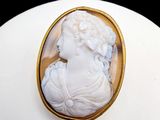 une photo d'une femme portant une robe blanche et une broche en or