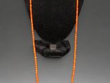 an orange beaded necklace on a black mannequin