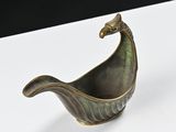 a small bronze boat shaped object on a white surface