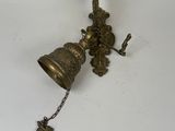 a brass bell hanging from a hook on the wall