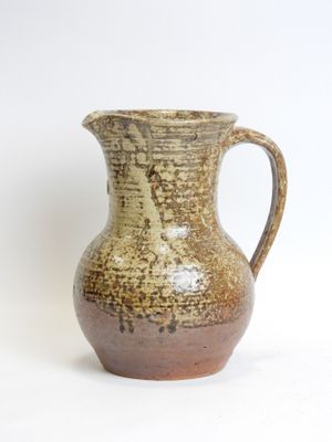 a brown vase with a handle sitting on a white surface