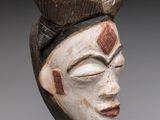 une image représentant un masque en bois posé sur un socle, sur fond gris
