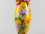 yellow vase with purple flowers on it sitting on a white surface