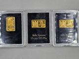 three gold bars in plastic cases on a white surface