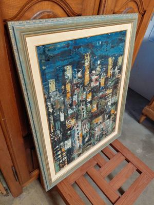 painting of a cityscape in a frame sitting on a wooden chair