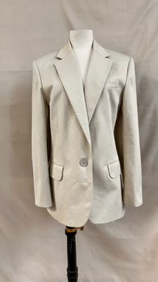 un blazer beige sur un mannequin, devant un fond blanc