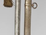 a silver object with a metal handle and a bell hanging from it ' s side