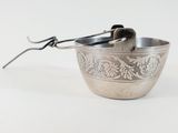 a silver bowl with a spoon in it on a white surface