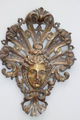 une plaque en or sur laquelle est représenté un visage, posée sur un fond blanc
