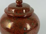 a red vase with a lid sitting on a white surface