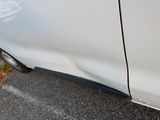 a white car that has been dented and is parked on the side of the road