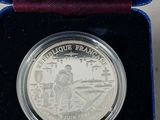 a silver coin in a blue box with a purple ribbon