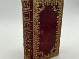 an old book with gold trimming and a red cover on a white surface