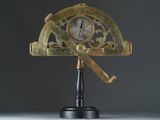 un compas doré posé sur un socle noir, sur lequel se trouve une horloge dorée