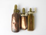 trois gourdes anciennes en laiton sont alignées sur une surface blanche