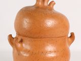 un petit vase marron muni d'un couvercle, posé sur une surface blanche