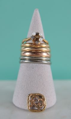 three gold and silver rings on a white cone with a turquoise background
