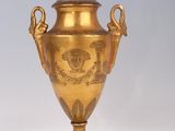 un vase doré posé sur un socle noir, sur fond blanc