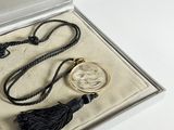 a necklace with a coin and a tassel in a box