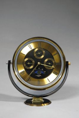 une horloge dorée et noire posée sur un socle, sur une surface blanche