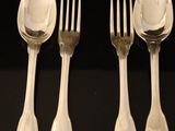four silver spoons and a fork are lined up on a black surface
