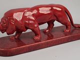 statue d'un lion rouge posée sur un socle en bois, sur fond gris
