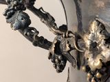 a silver vase that has a bunch of grapes on it