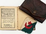 an old book with arabic writing and a leather wallet on a white surface