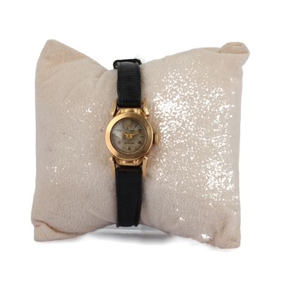 une montre en or avec un bracelet noir posée sur un oreiller