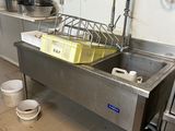 un évier en acier inoxydable dans une cuisine professionnelle, avec des casseroles et des poêles posées sur le plan de travail
