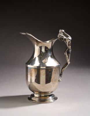 a silver pitcher sitting on a table with a dragon on it