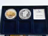 two silver and gold coins in a blue box on a white surface