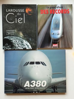 trois livres posés sur une table, avec un avion et un train en arrière-plan