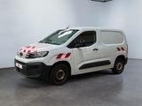 La camionnette blanche est garée dans une grande pièce ; elle porte une bande rouge et blanche sur le côté.
