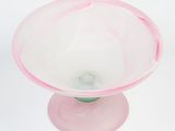 a pink glass bowl with a green base on a white surface