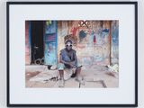framed photograph of a man sitting on the ground in front of a building